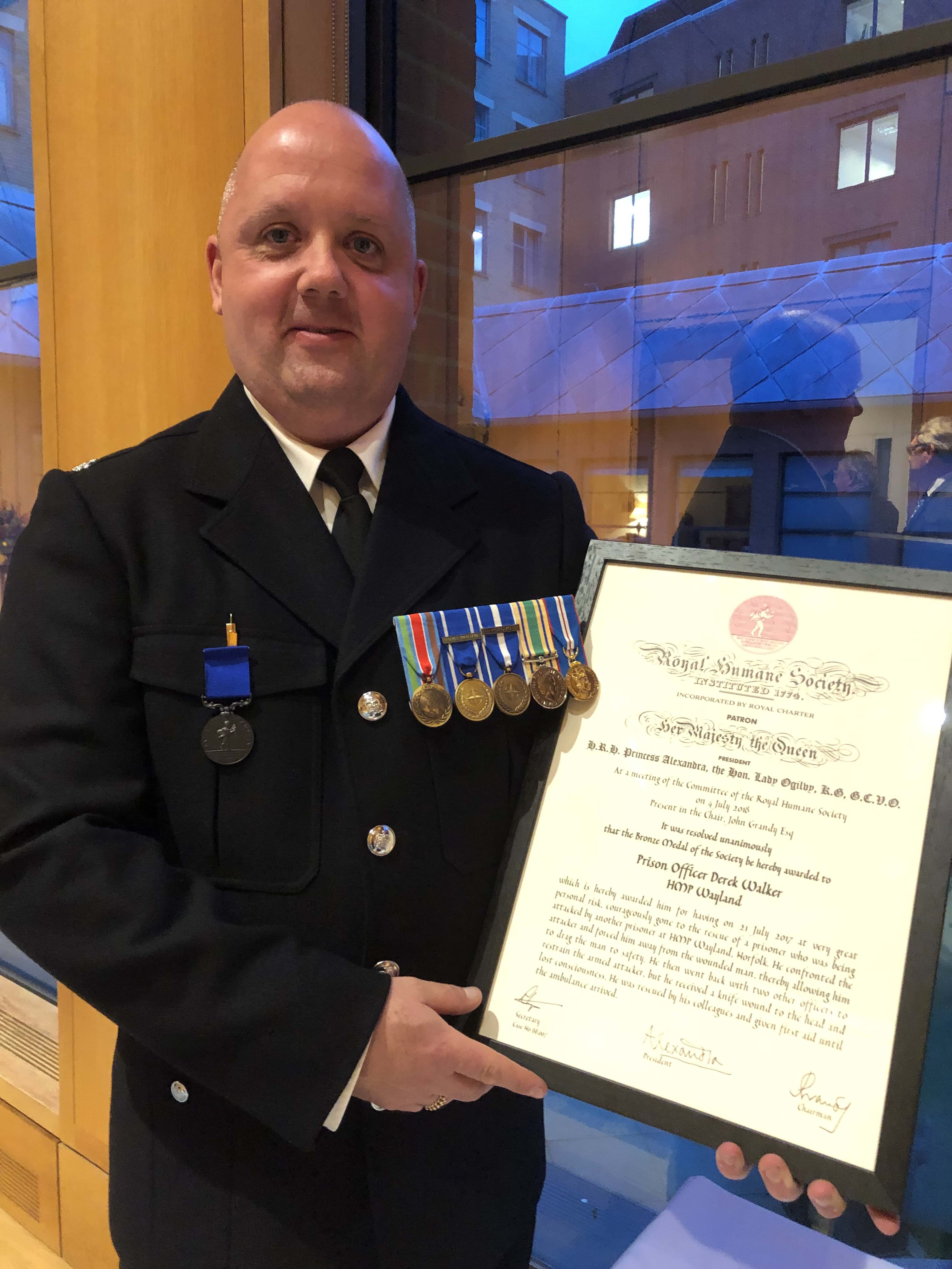 A prison officer holding a certificate for bravery